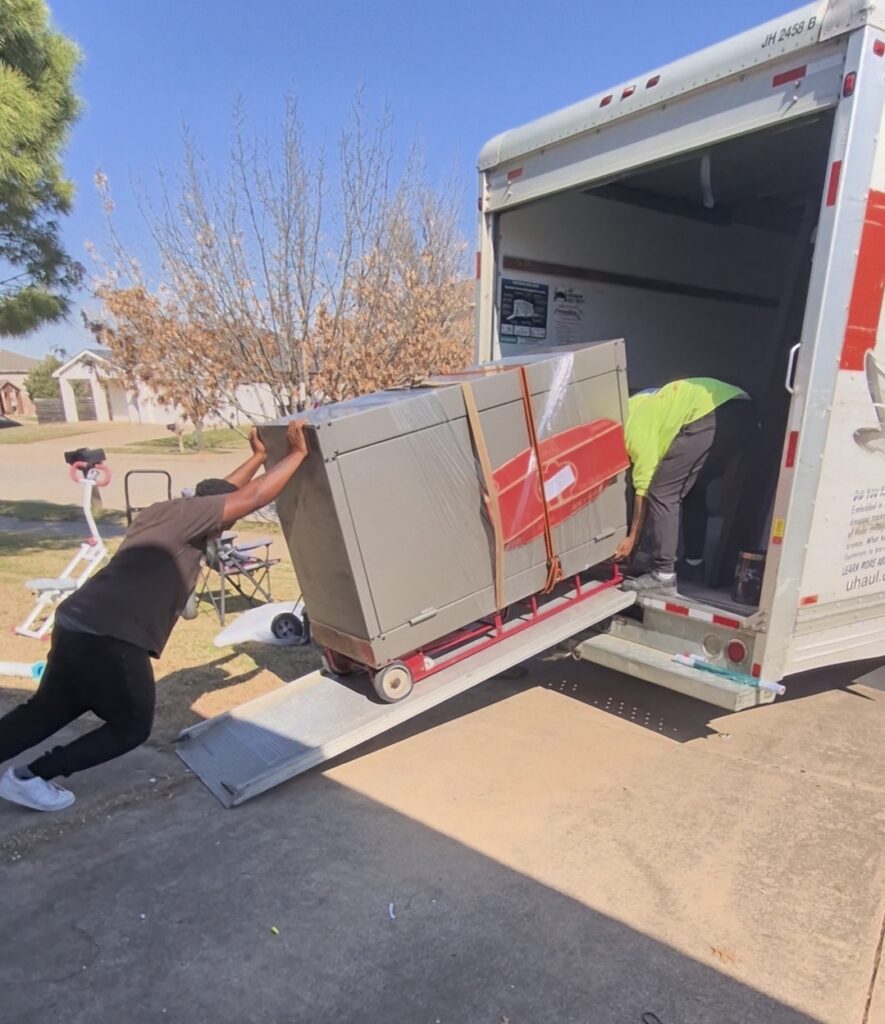 Two movers pushing a large, heavy safe into a moving truck.