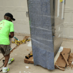 Movers carefully transporting a large refrigerator/freezer from a driveway into a residential home in the Keller and Fort Worth area