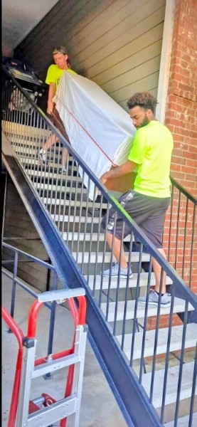 Two team members from Sky Is The Limit Moving carefully carrying a wrapped dresser down a staircase during a apartment move in Fort Worth, Texas.