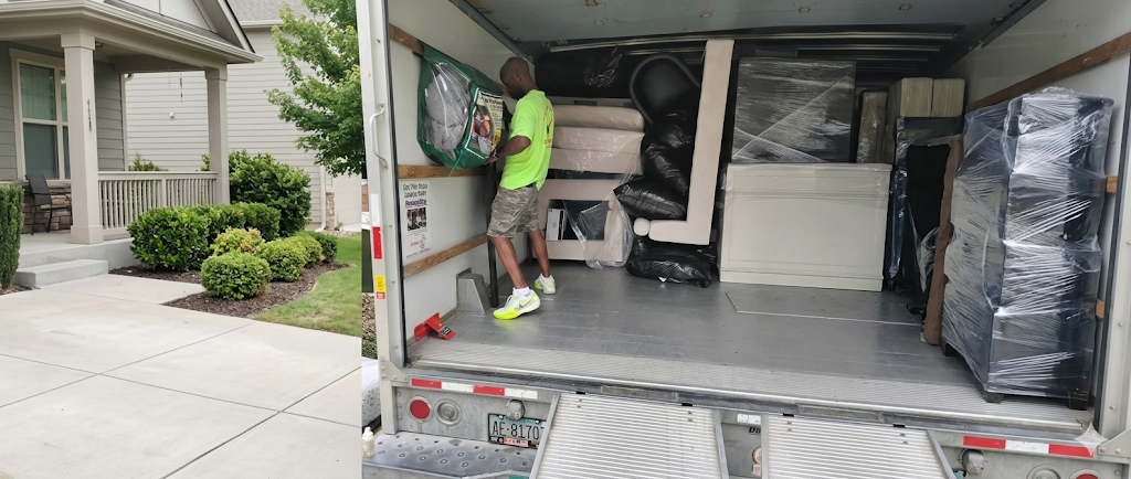A professional mover in a high-vis yellow shirt loads a protected green storage bag into a tightly packed moving truck in Dallas. A well-landscaped house porch is visible to the left.